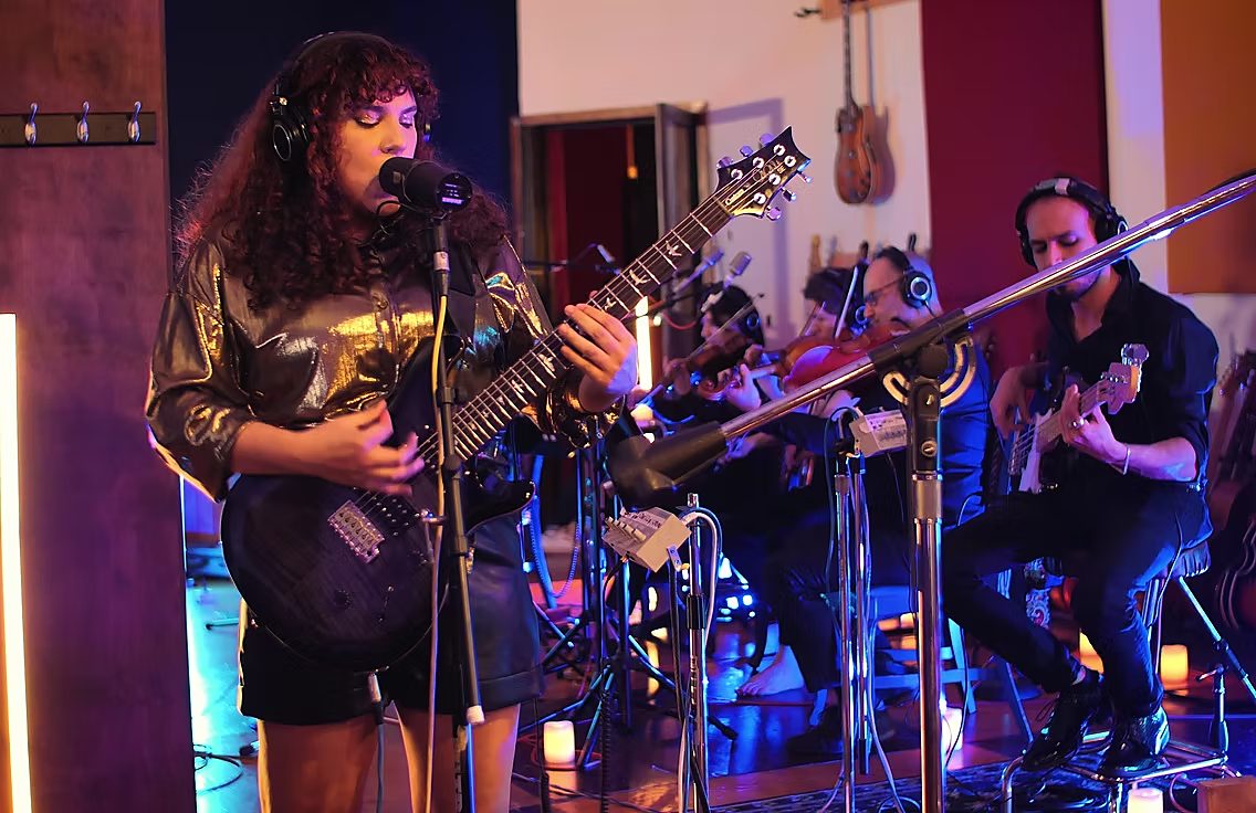 Singer with guitar alongside strings and bass